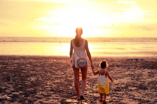 Mom and child walking toward ocean during sunset